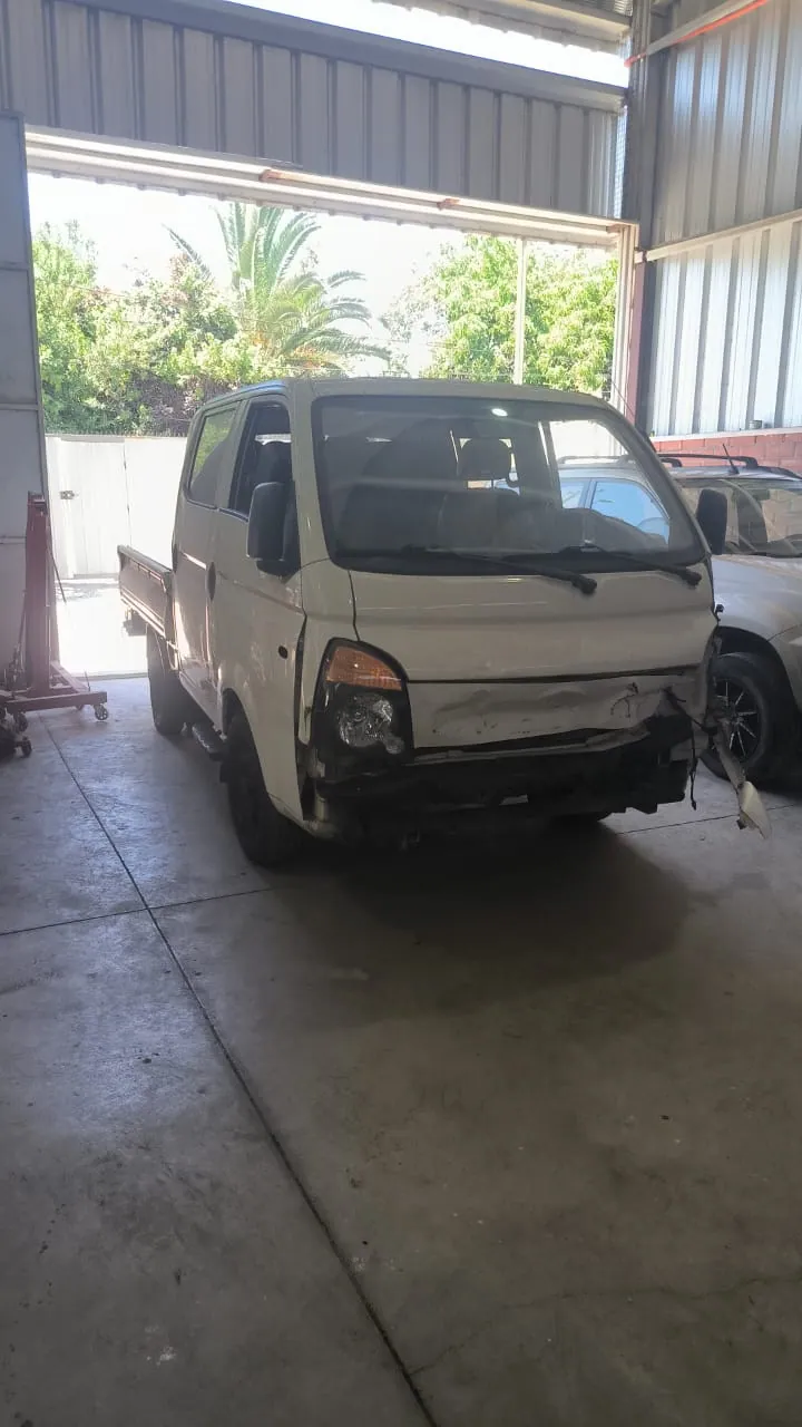 Hyundai H100 blanca con golpe frontal dentro del taller de airbags